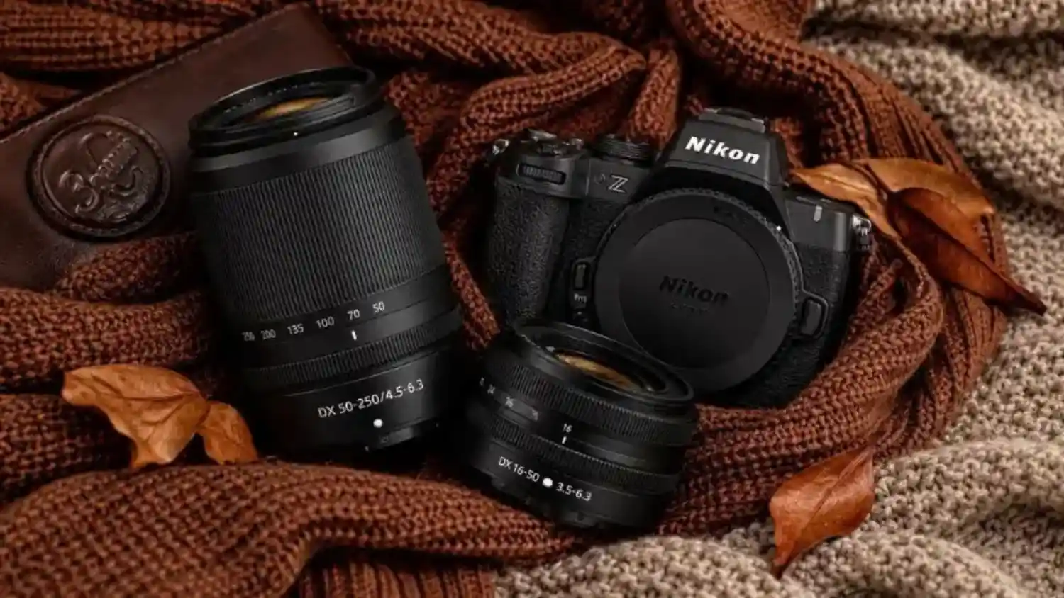 Nikon Z mirrorless camera and two zoom lenses arranged on brown knit fabric with dried autumn leaves.
